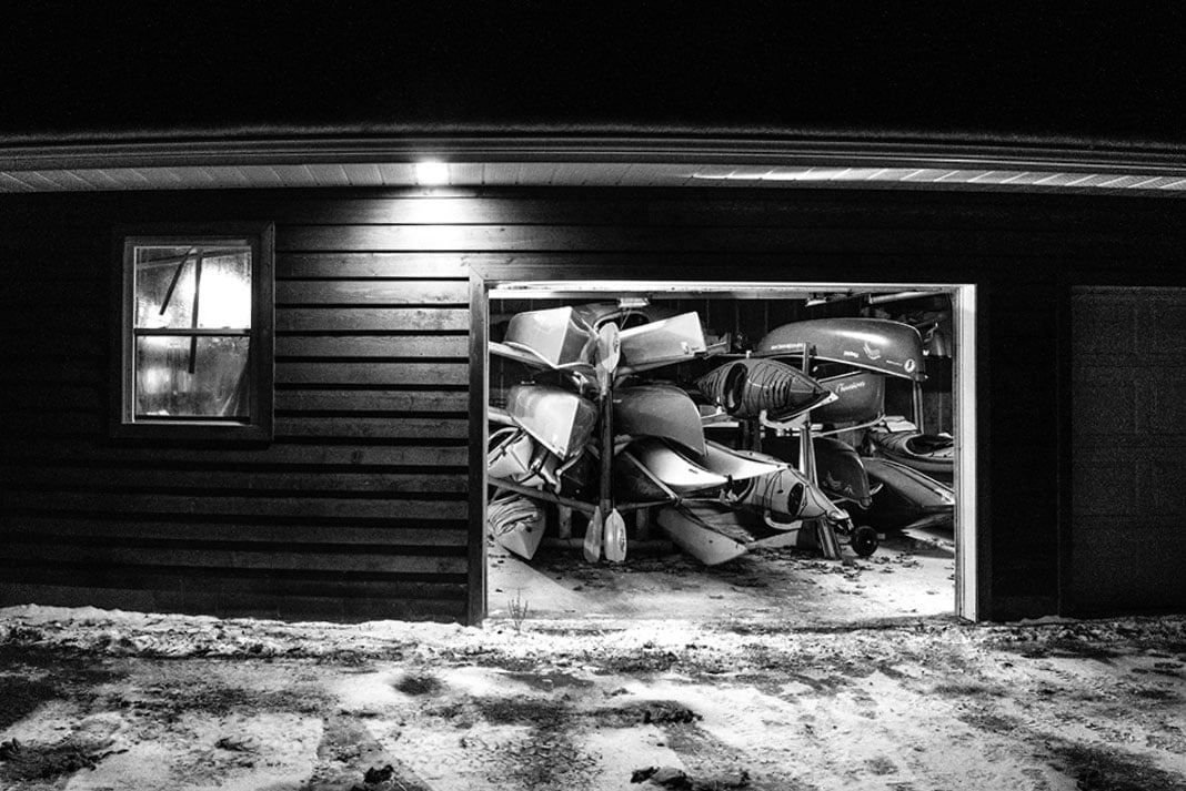 black and white photo looking into a garage full of paddling gear at night with garage door open
