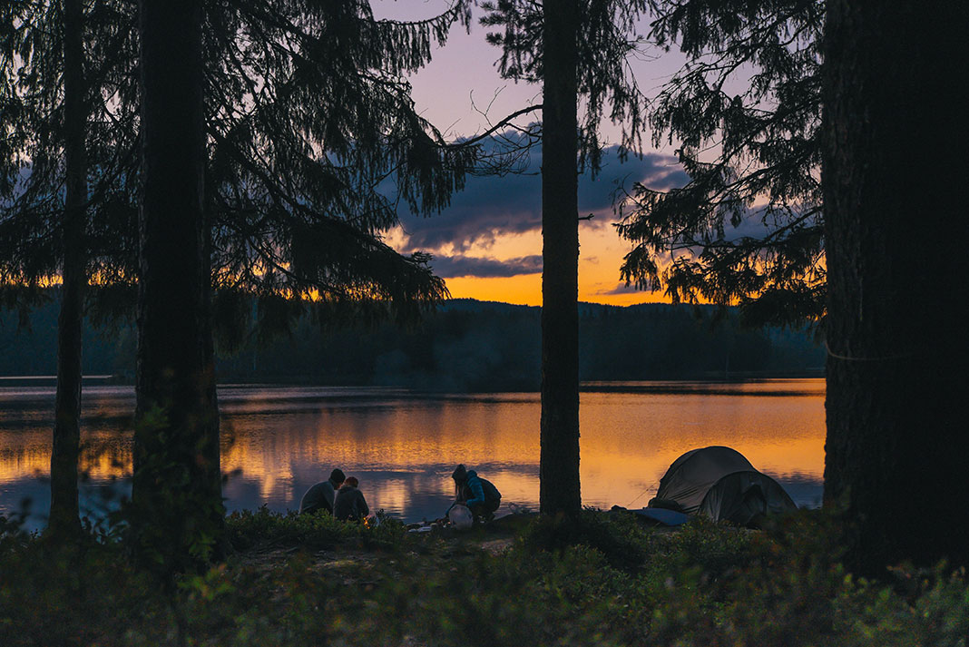 a family crouches by a campfire at a dusky lakeside campsite