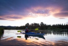 The Beginner’s Guide To Kayaking Woman paddling a kayak on a lake at sunset