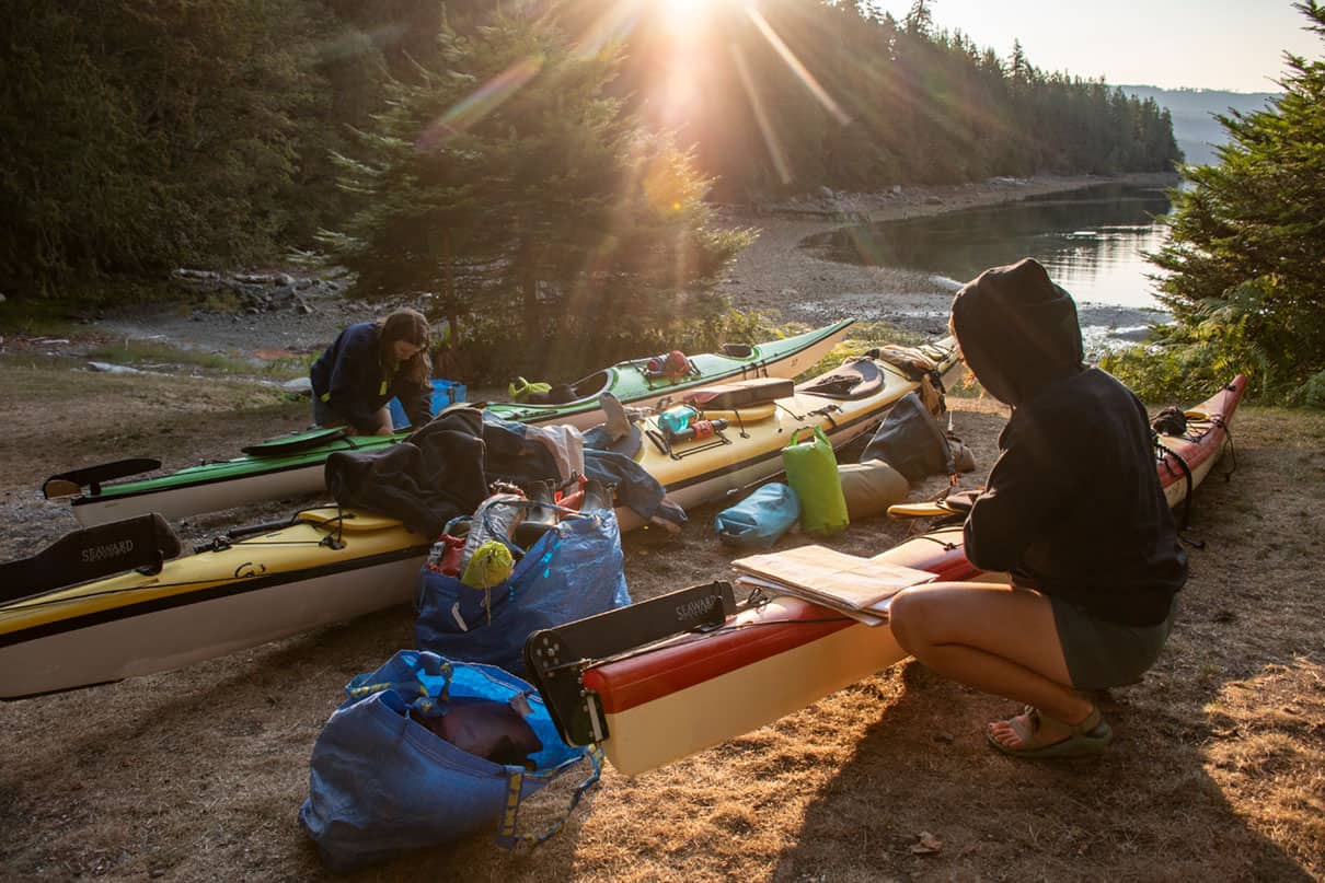 two people pack their kayaks in the sun while kayak camping