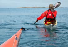 How To Kayak Tow Your Friends Out Of Trouble a person paddles toward an island while towing another sea kayak