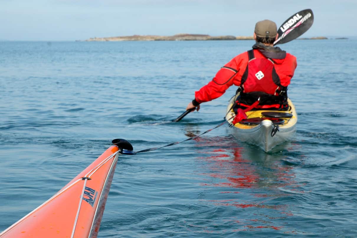 a person paddles toward an island while towing another sea kayak