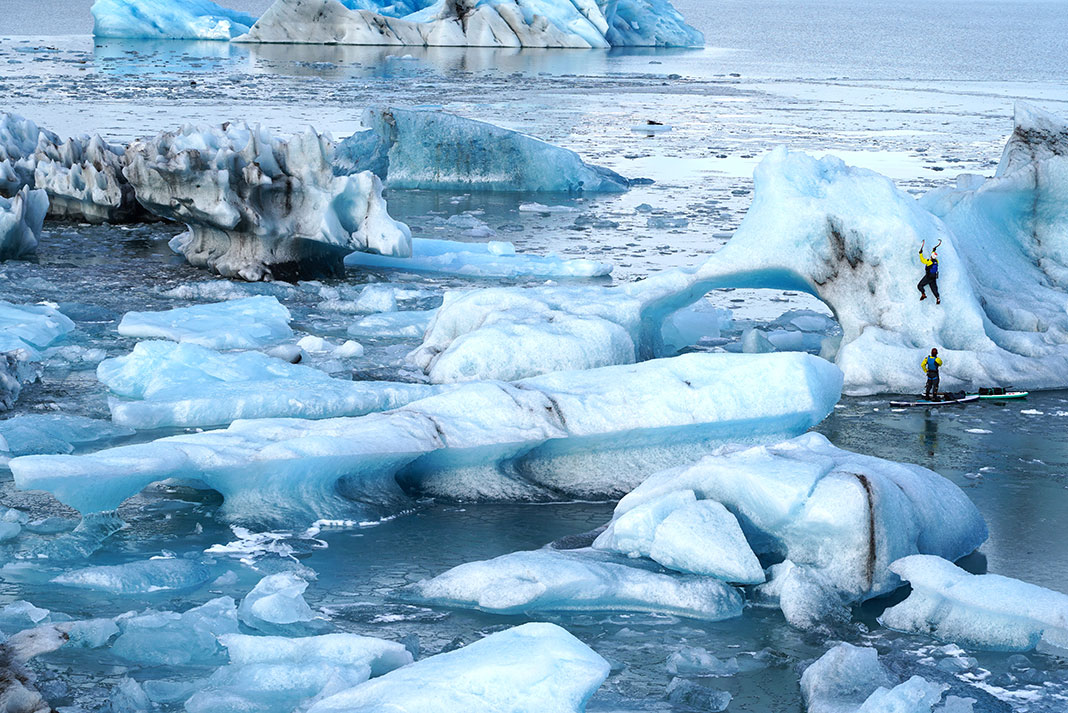 two people paddleboarding and climbing icebergs off the Iceland coast