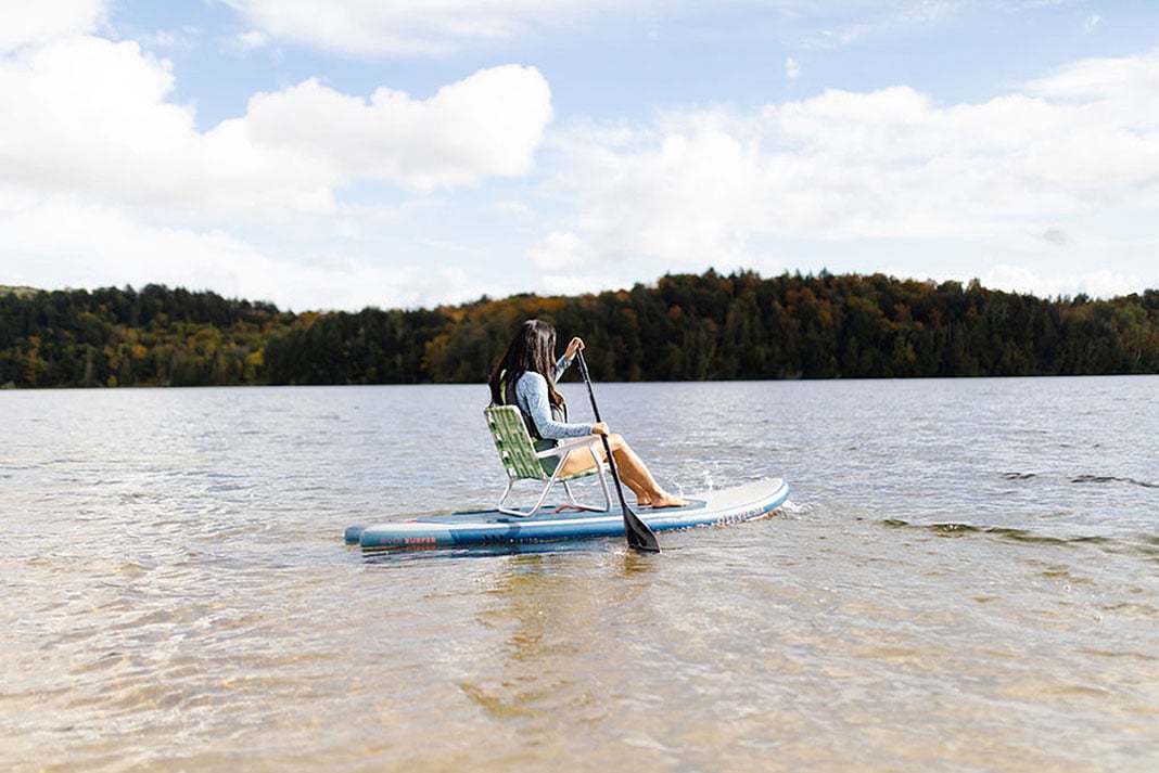 in one of several new trends in the sport, a woman sits down on a lawn chair while paddleboarding