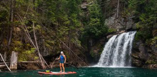 A paddleboarder stands next to a waterfall