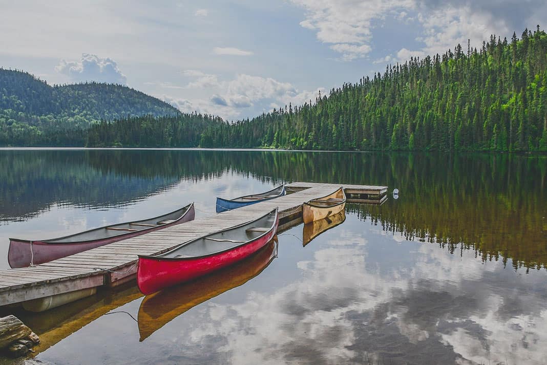 Four canoes tied to dock on a lake with trees and hills in background