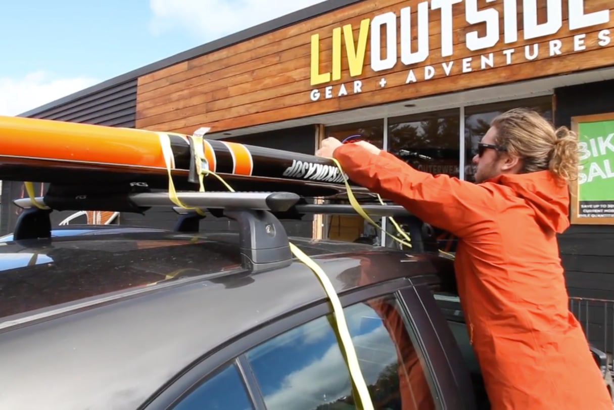 Persons using cam strap to show how to transport a paddleboard.