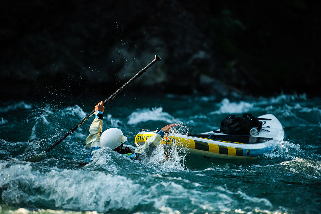 man swims in whitewater beside a paddleboard connected to him with a SUP leash