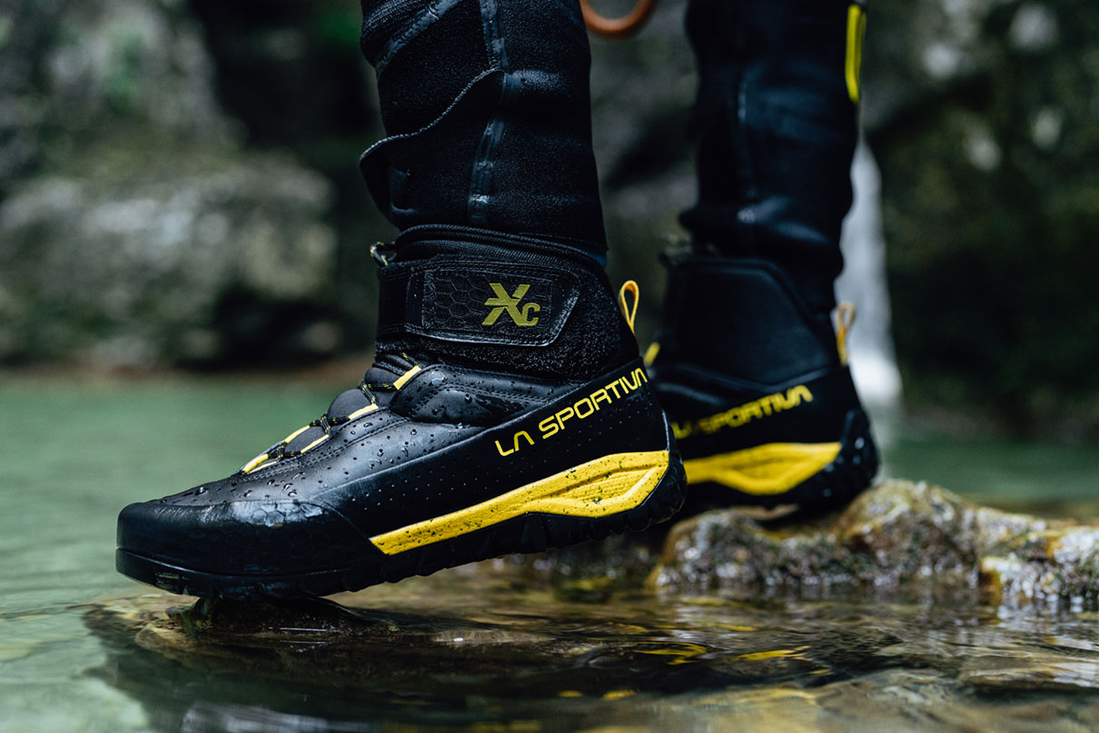 Close-up of a person wearing La Sportiva TX Canyon water shoes while standing on a rock in view of a waterfall.