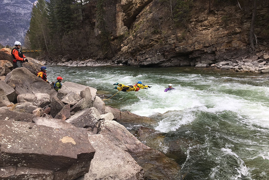 a whitewater rescuer leaps into the river to save a kayaker using rescue gear
