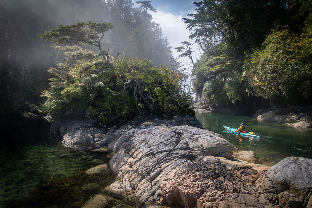 a person kayaking through a rocky, lush wilderness scene