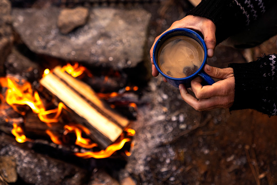 overhead photo of a person holding a mug of coffee over a campfire